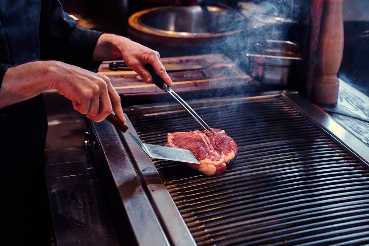 Close-up image of a cooking delicious meat steak on a grill in a restaurant kitchen.